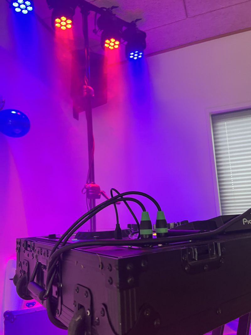 DJ-pult i flightcase under en lysbro med røde og blå lamper, rummet badet i violet lys