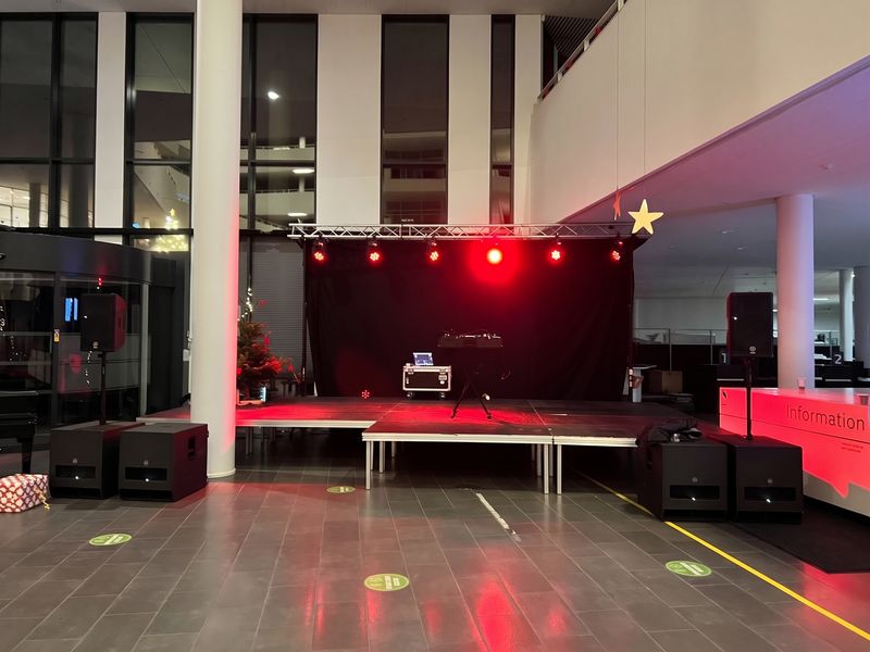 DJ-opstilling på en scene med rødt lys fra lysbroen i et stort atrium til en firmafest