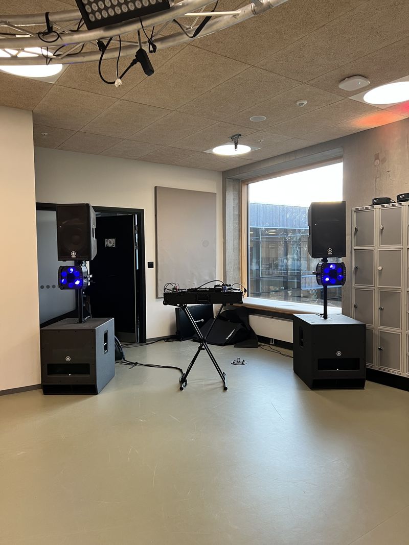 Opstilling til skolefest med højttalere på subwoofere, blå lyseffekter og DJ-pulten i midten