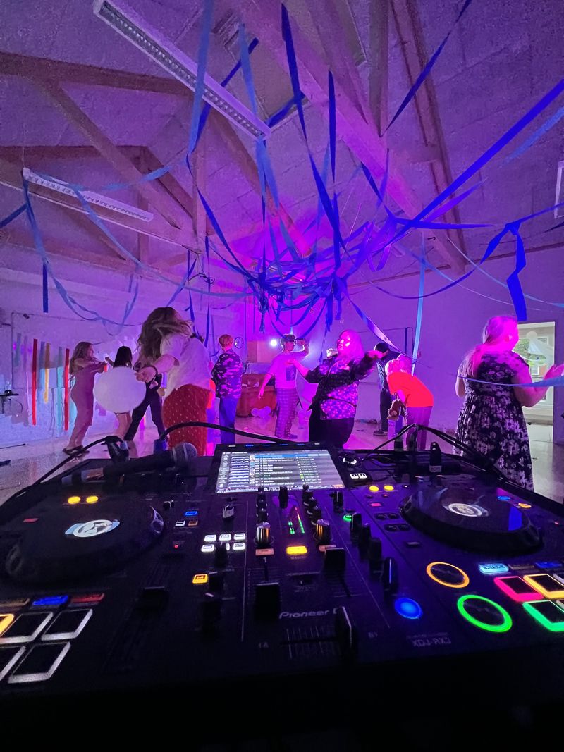 Set bag DJ-pulten: unge danser under blå serpentiner i lilla lys
